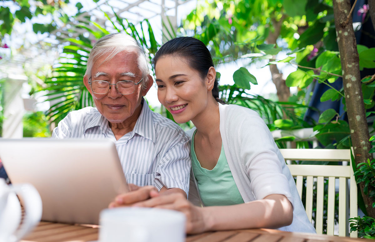 An instructor patiently helping an older woman use her laptop at home.